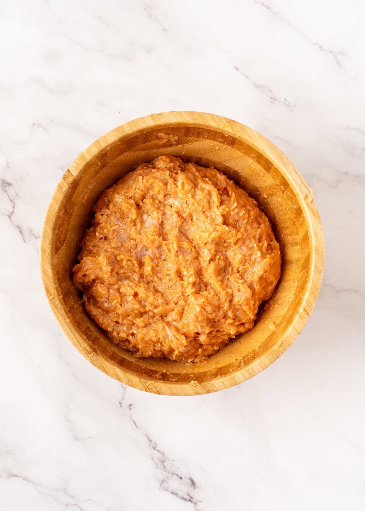 A wooden bowl filled with raw ground meat.