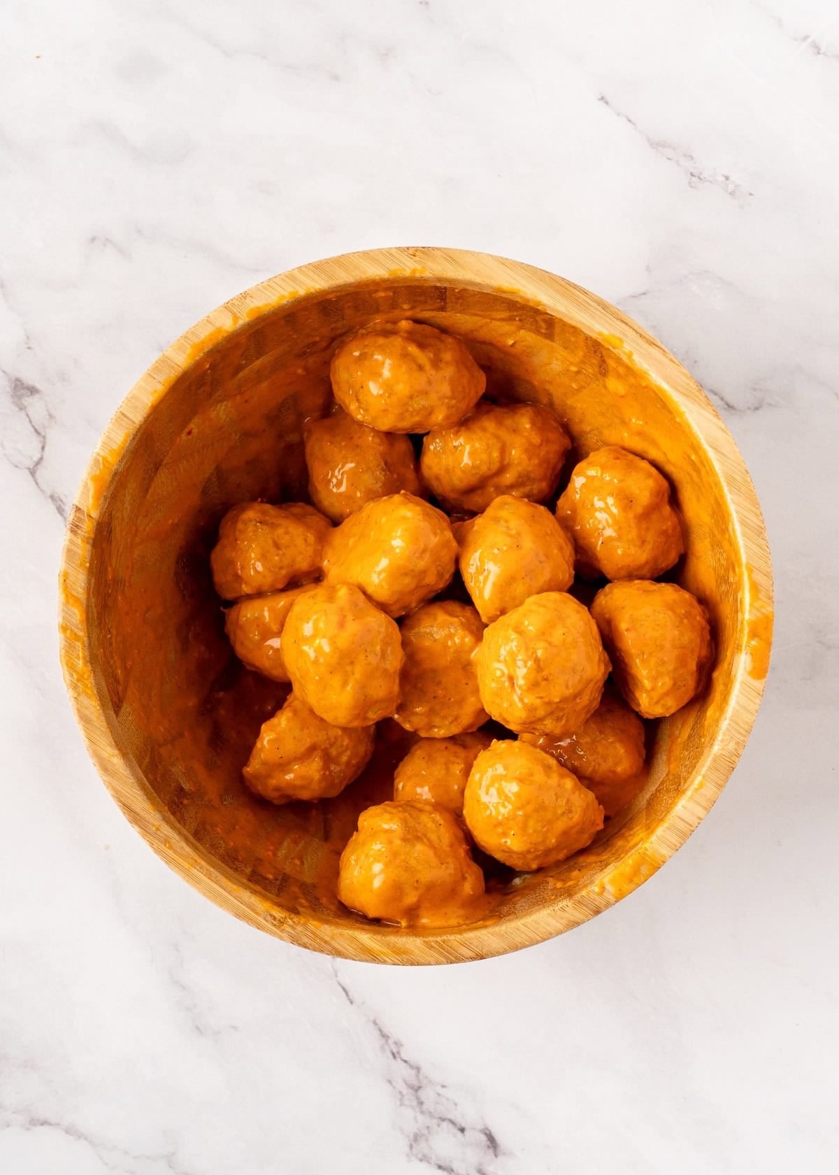 Meatballs coated in a thick orange sauce inside a wooden bowl.