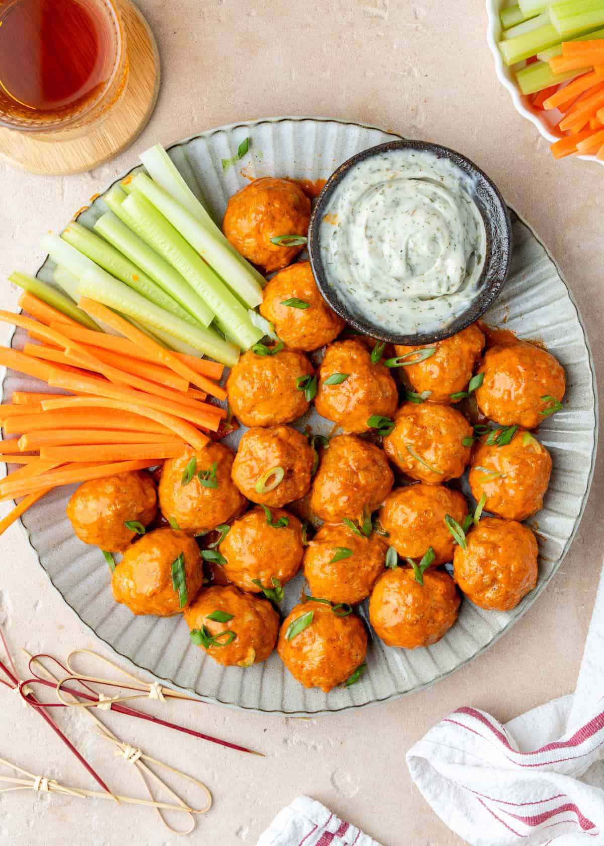 Buffalo chicken meatballs on a plate with celery sticks, carrot sticks, and ranch dip.